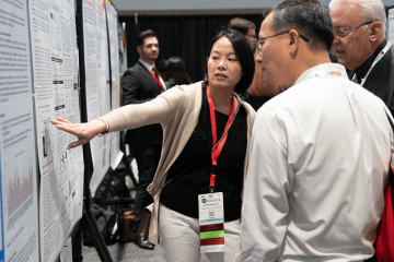 Poster presenter at conference pointing out sections on poster to attendees